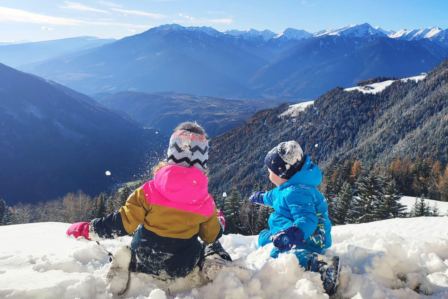 Zwei Kinder spielen im Schnee vor einer atemberaubenden Berglandschaft - Scheaterhof