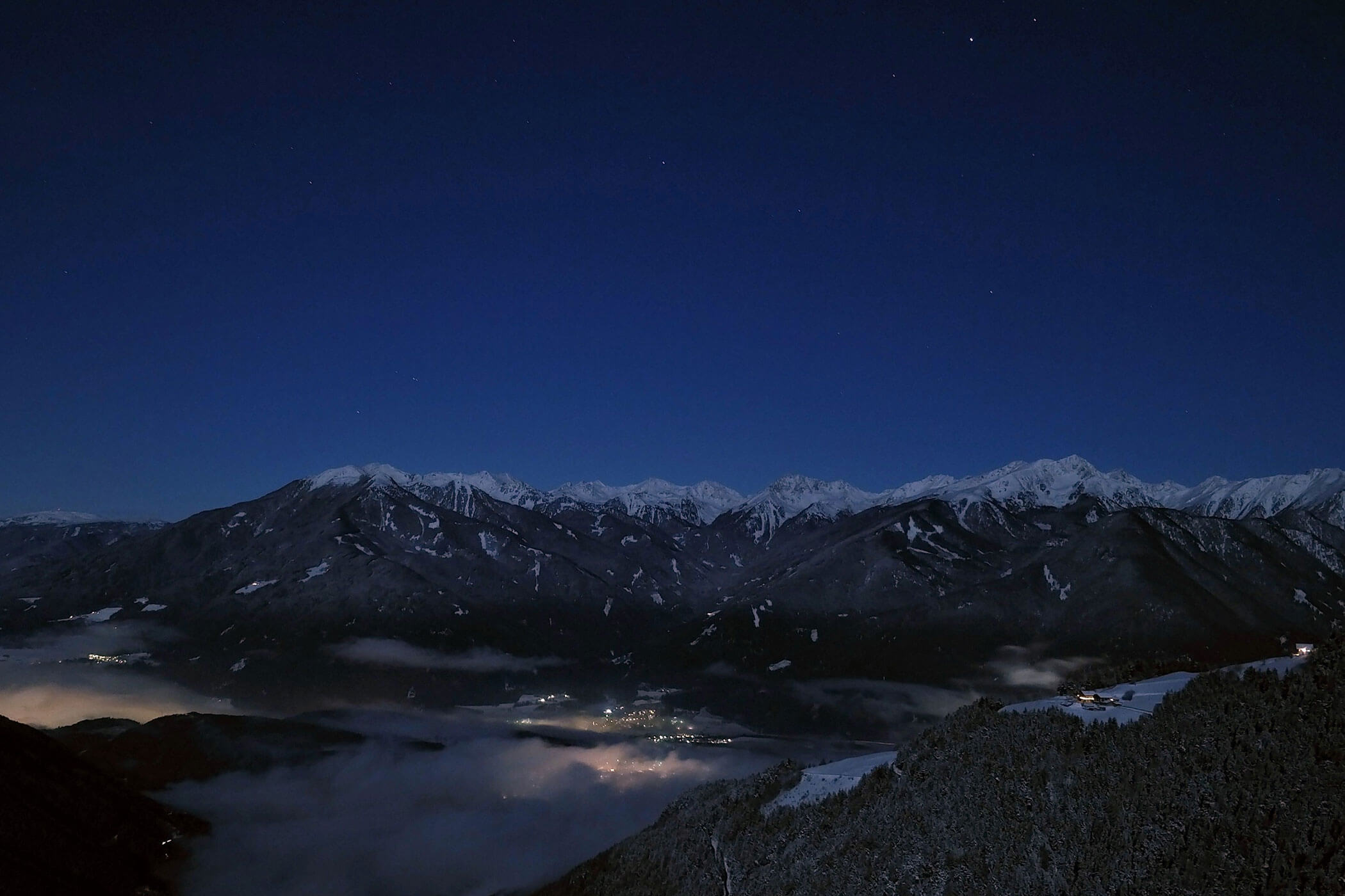 Die verschneiten Berge und das leuchtende Dorf darunter - Scheaterhof