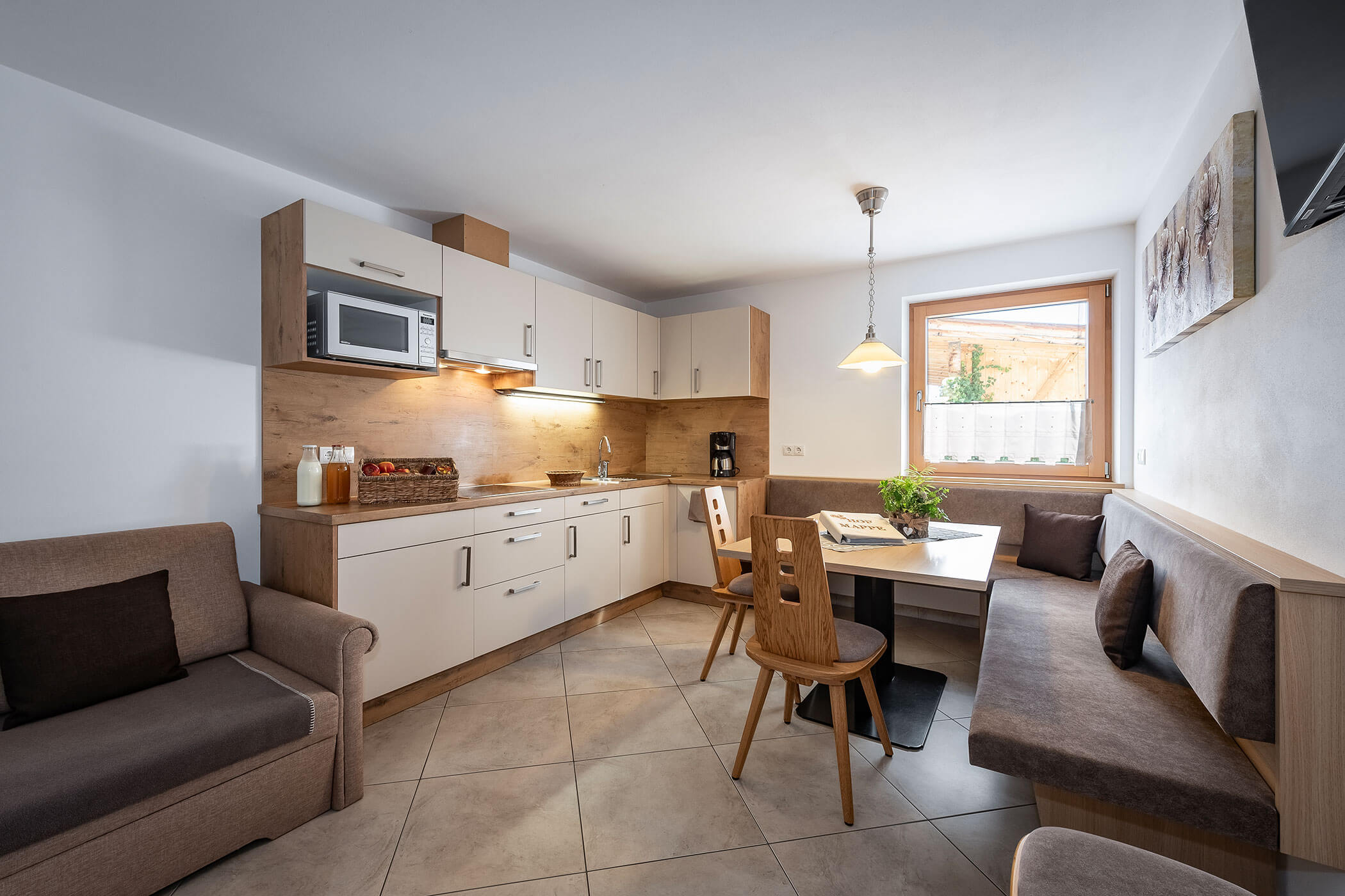 Wohnküche in der Ferienwohnung Peitlerkofel mit weißer Küche, Eckbank, Tisch und Sofa - Scheaterhof